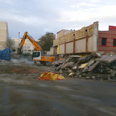 Une excavatrice démolit un bâtiment en ruines, laissant un site de débris et de terre.