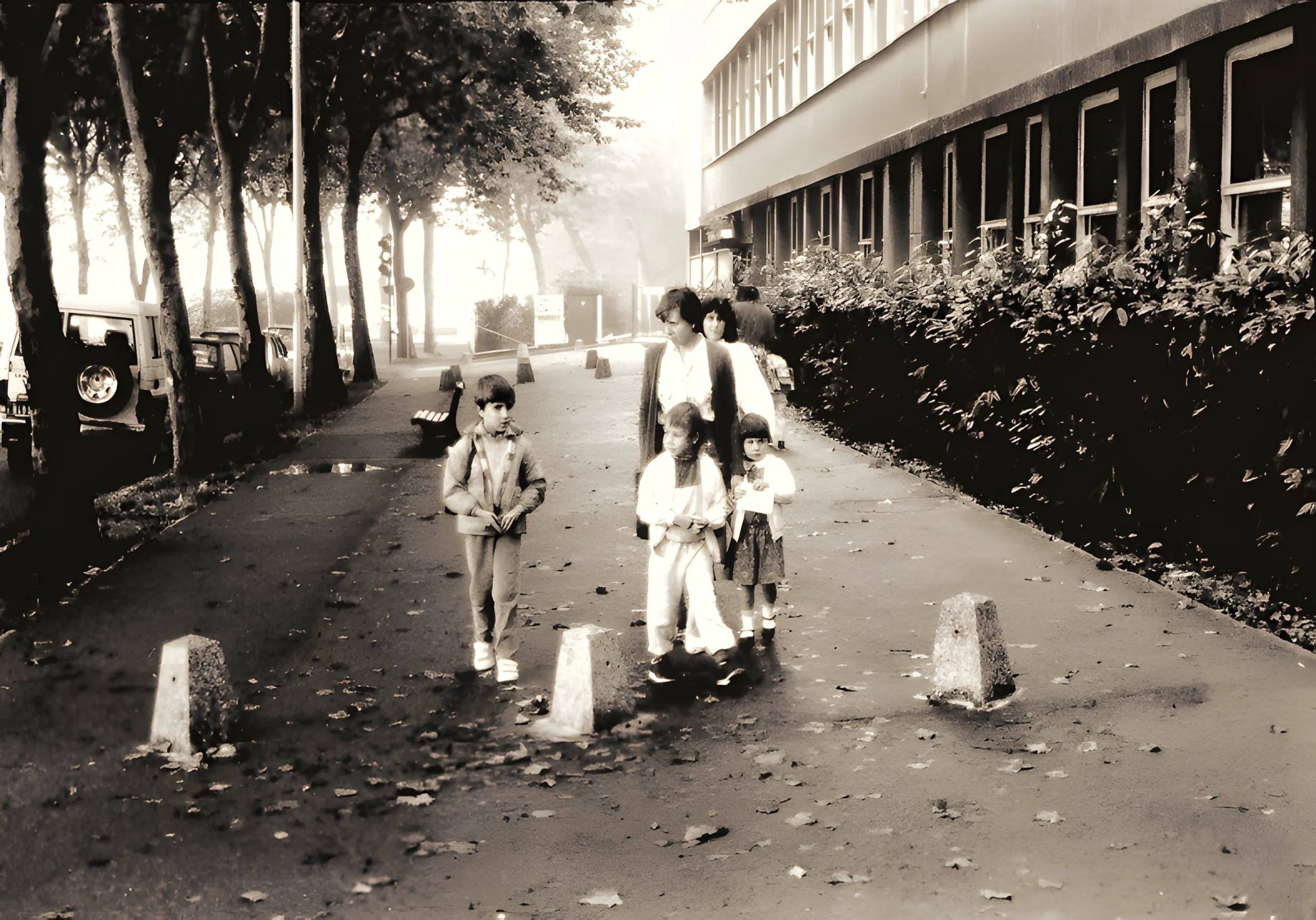 Des enfants accompagnés de leur mère marchent le long d'un trottoir en direction d'une école.