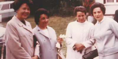 Quatre femmes portant des robes blanches sourient dans un jardin.