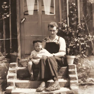 Un homme et un jeune garçon assis sur les marches d'une maison, dans un décor champêtre.