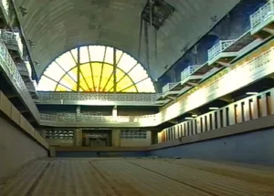 Vue intérieure d'une piscine abandonnée avec une lucarne ensoleillée et des baldaquines délabrées.