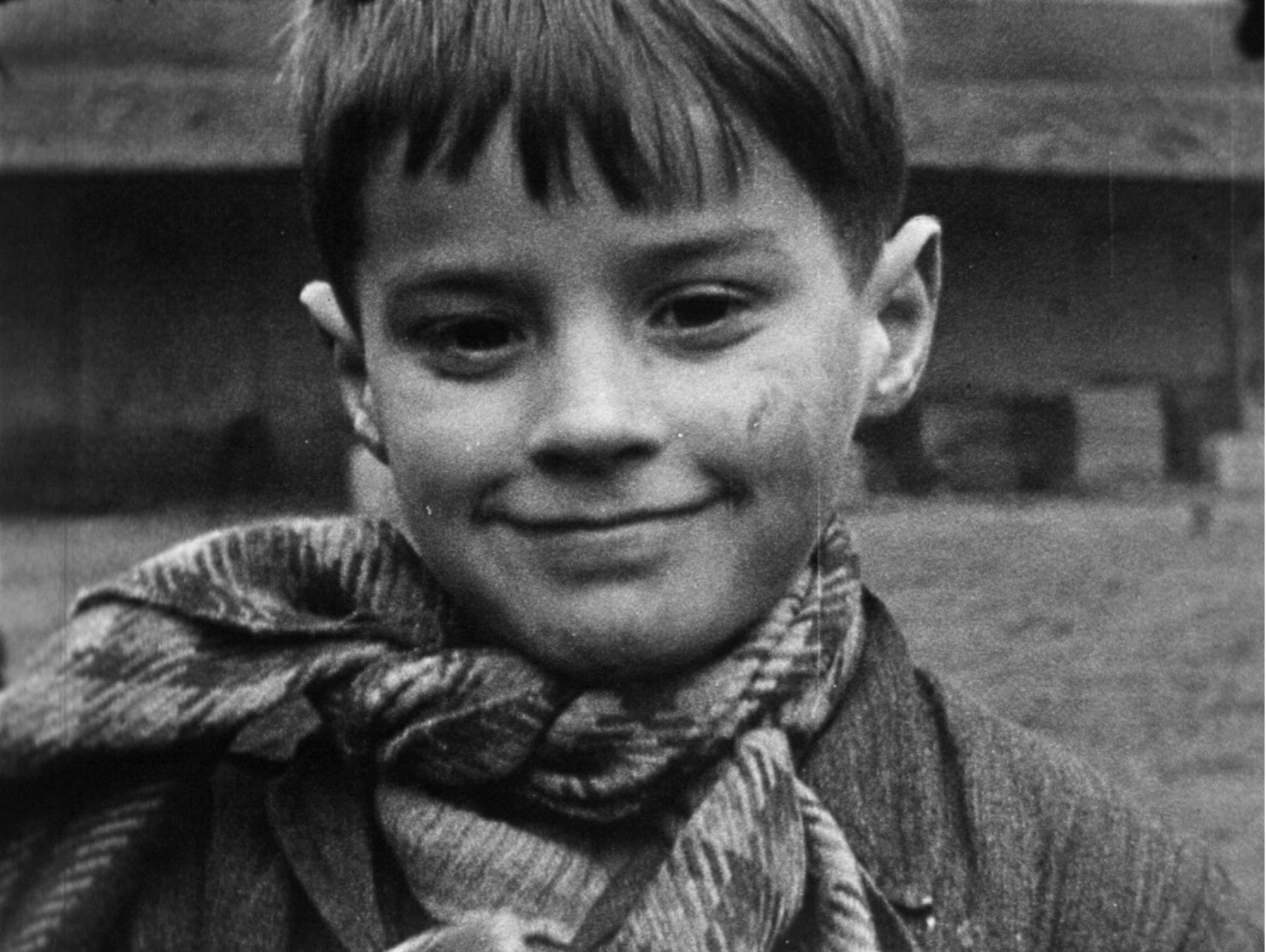 Un jeune garçon souriant, au regard vif, vêtu d'un châle, dans une ambiance en noir et blanc.
