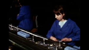 Deux ouvrières travaillent sur une machine complexe dans un atelier sombre.