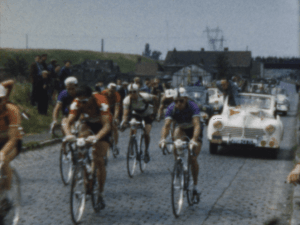 Cyclistes en compétition sur une route, suivis par une voiture de reconnaissance lors d'une course.