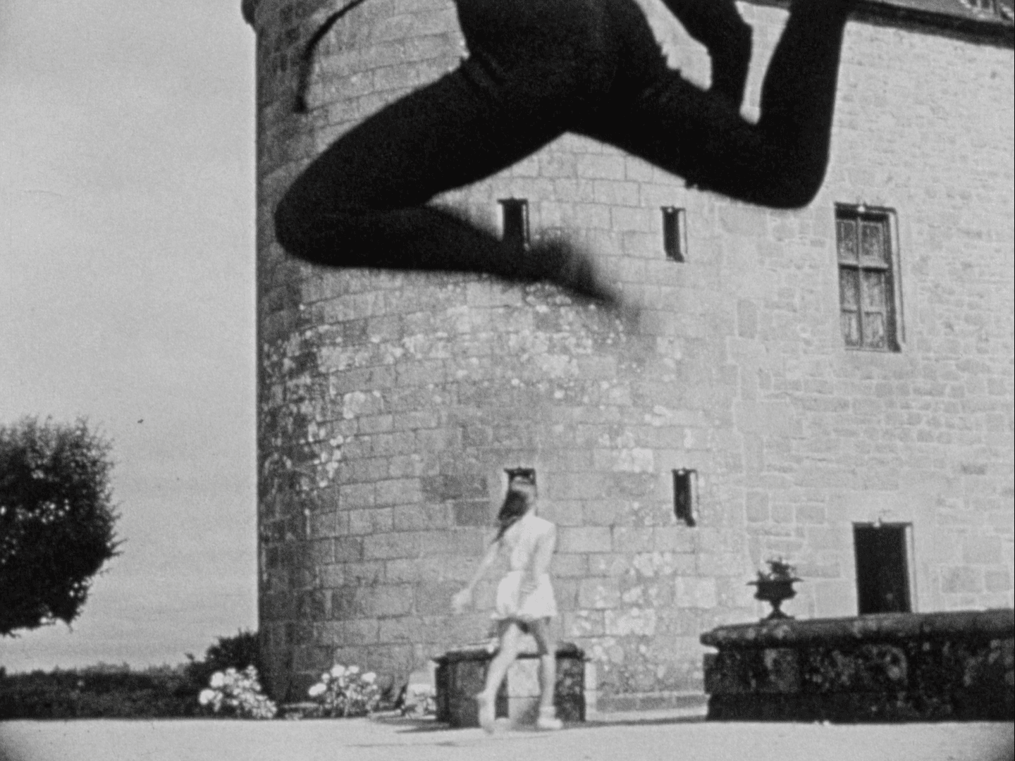 Une silhouette imposante projette une ombre sur un château, une femme se tient devant.