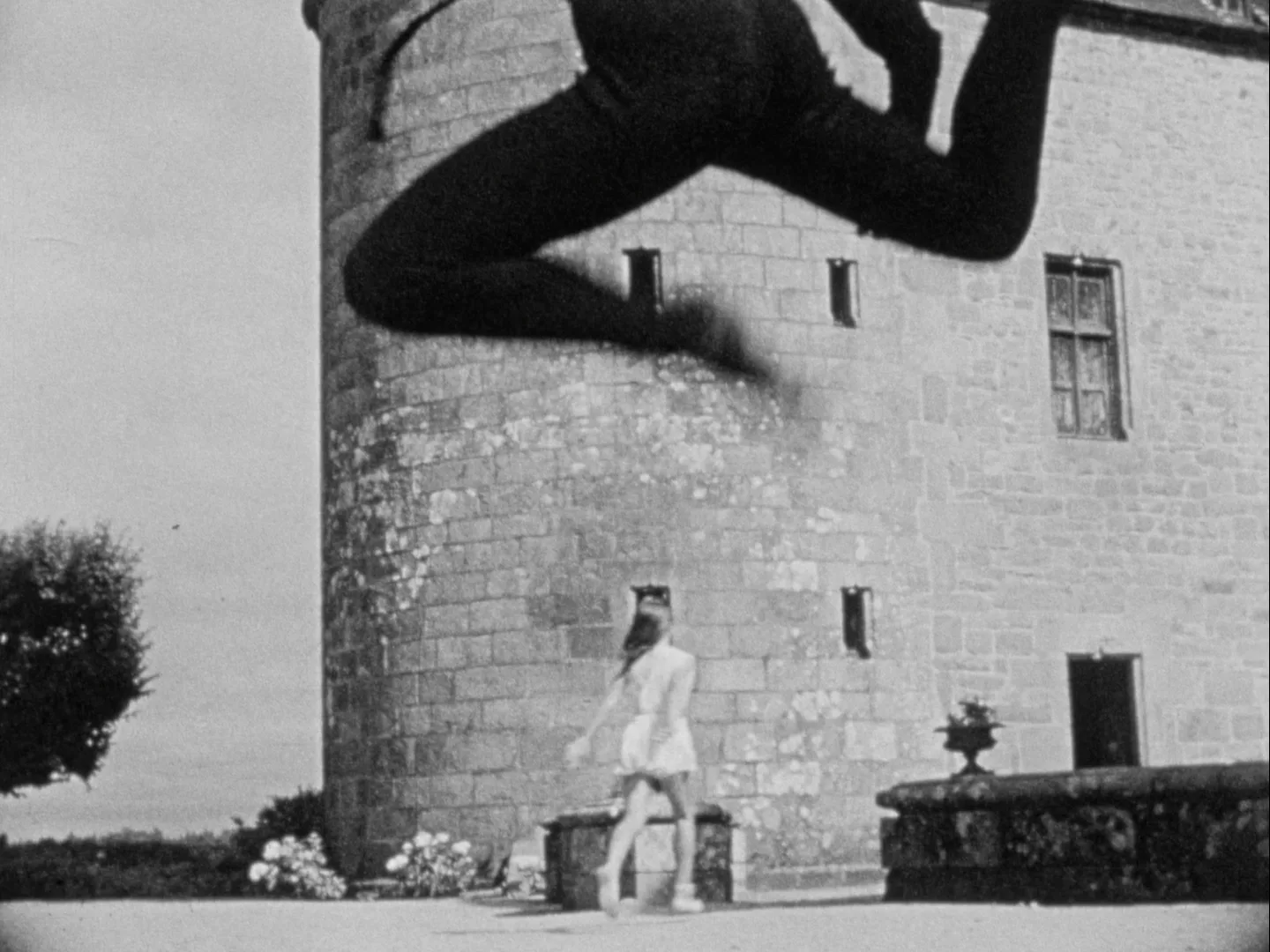 Une silhouette imposante projette une ombre sur un château, une femme se tient devant.
