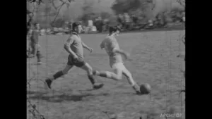 Deux joueurs de football s'affrontent sur un terrain en pleine action, en noir et blanc.