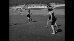 Trois personnes en maillots de bain jouent sur une plage en noir et blanc.