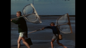 Deux enfants courent sur une plage avec des filets à papillons.
