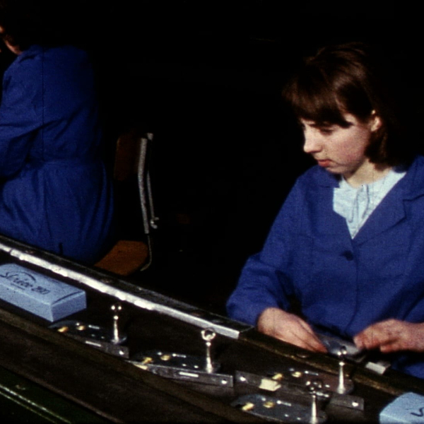Deux ouvrières travaillent sur une machine complexe dans un atelier sombre.