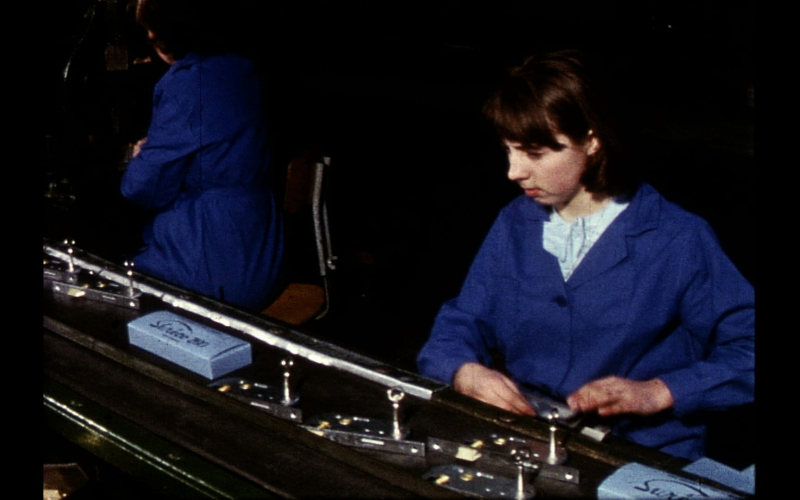 Deux ouvrières travaillent sur une machine complexe dans un atelier sombre.