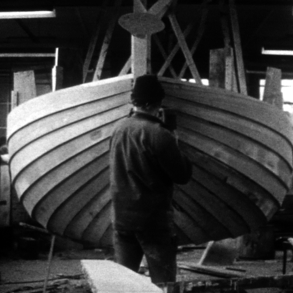 Photographie en noir et blanc de deux charpentiers de marine construisant la coque d'un bateau en bois.