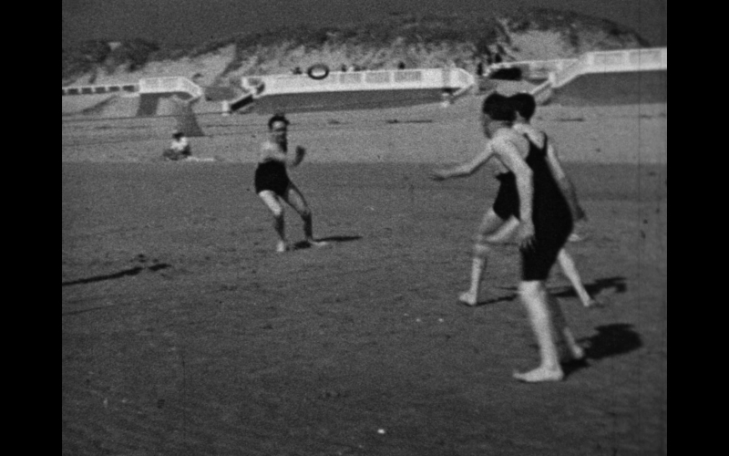 Trois personnes en maillots de bain jouent sur une plage en noir et blanc.