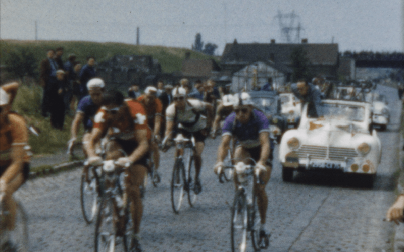 Cyclistes en compétition sur une route, suivis par une voiture de reconnaissance lors d'une course.