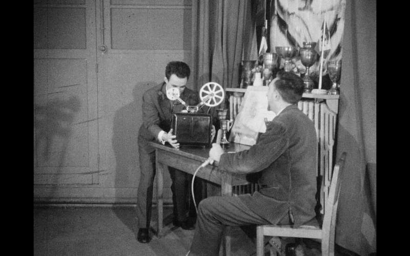 Deux hommes utilisent un projecteur de cinéma dans un décor d'époque.