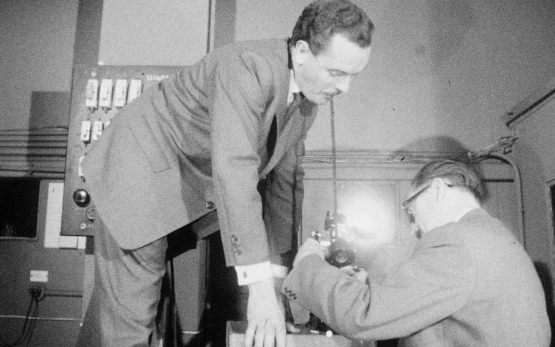 Deux hommes travaillent sur un ordinateur ancien dans un laboratoire.