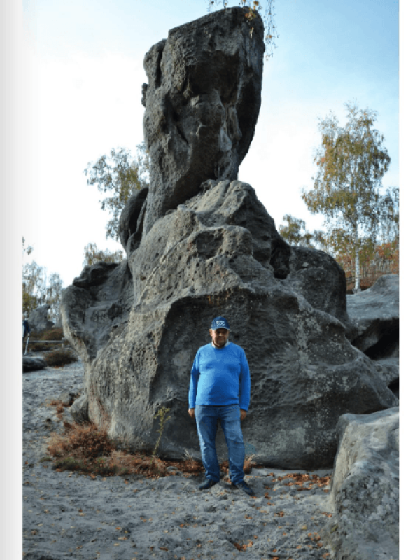 Un homme en pull bleu et casquette se tient debout devant une immense formation rocheuse sculptée.