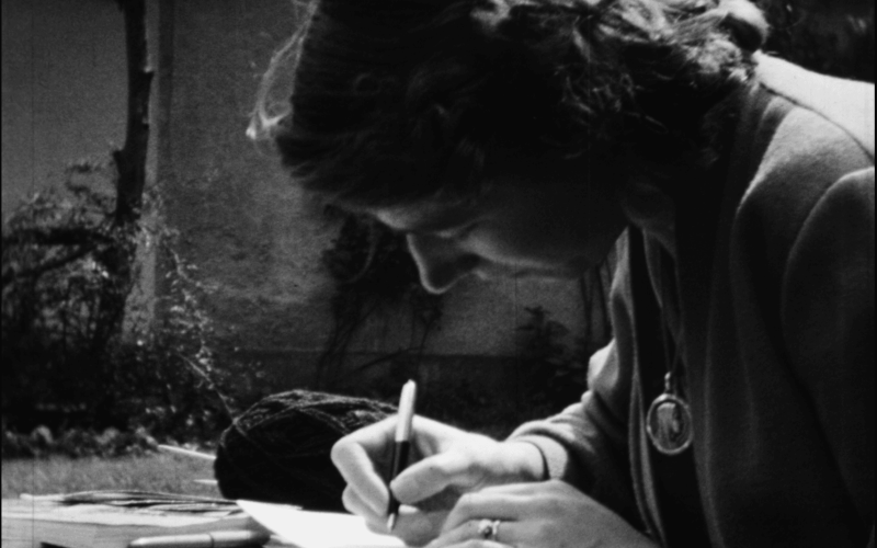 Photographie en noir et blanc d'une femme écrivant avec un stylo sur du papier à l'extérieur.