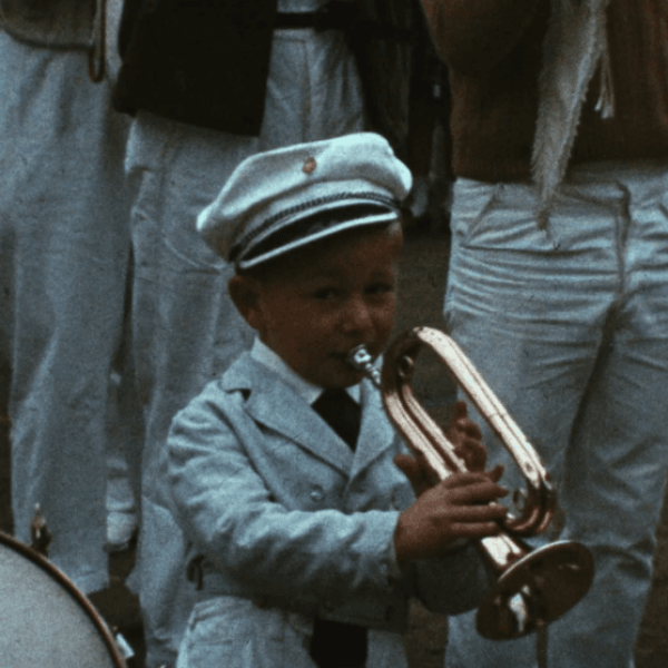 Un petit garçon en uniforme blanc et casquette joue de la trompette.