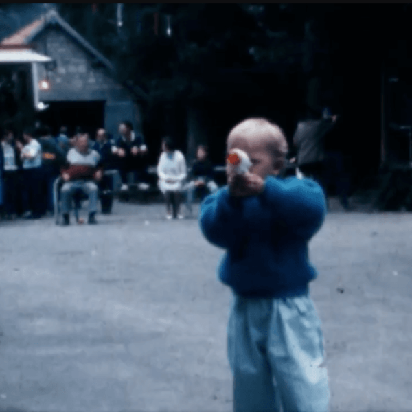 Un jeune enfant en pull bleu et pantalon clair se tient debout et porte un objet à sa bouche.