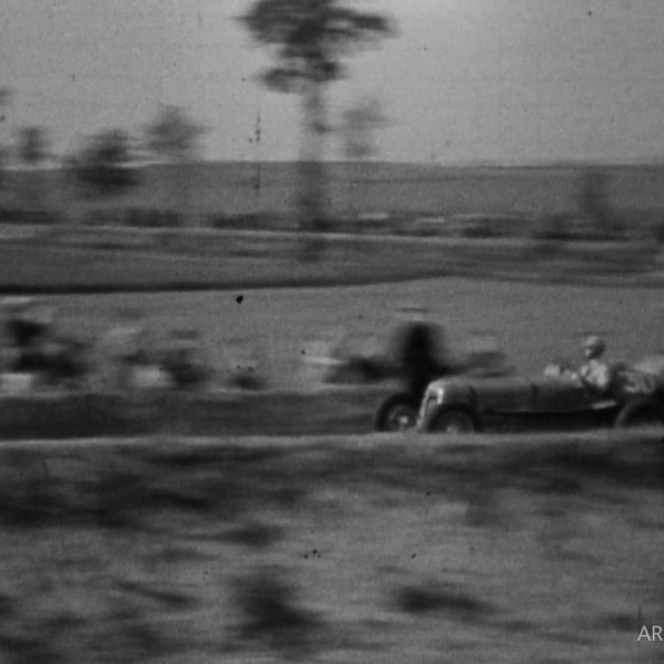 Une voiture de course ancienne et floue circule à grande vitesse sur un circuit en noir et blanc.