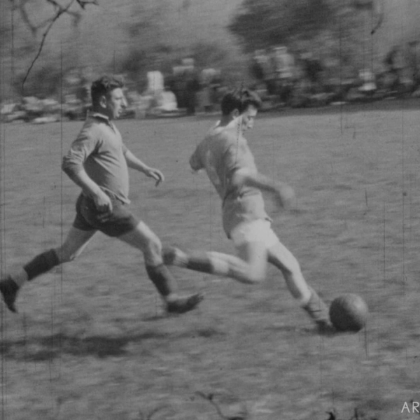 Deux joueurs de football s'affrontent sur un terrain en pleine action, en noir et blanc.