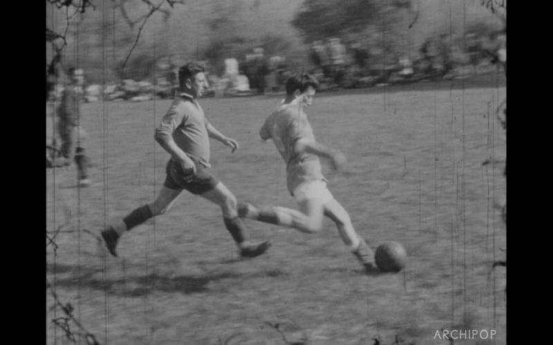Deux joueurs de football s'affrontent sur un terrain en pleine action, en noir et blanc.